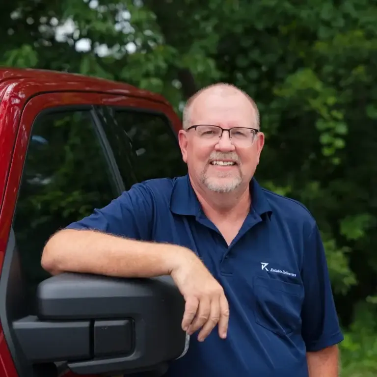 Bob, part of the Niagara delivery service team at Reliable Deliveries, stands beside the company red pickup truck.
