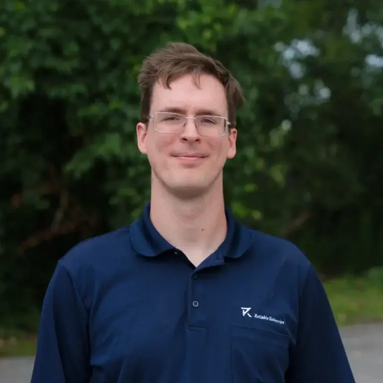 Sean, a Niagara delivery driver for Reliable Deliveries, wearing glasses in the company uniform.